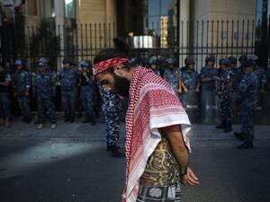 A Lebanese protester draped in a traditional Palestinian Keffiyeh scarf walks past a row of security forces during ongoing anti-government demonstrations in central Beirut  (AFP)