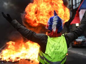 In this file photo taken on December 29, 2018 A "Yellow vest" (gilets jaunes) anti-government demonstrator holds up the French flag as he stands infront of a fire during protests in the western French city of Bordeaux. On November 17, 2018, 282,000 people according to the authorities, responded to a Facebook call, yellow vest on their backs, outside any political or trade union framework, and invested hundreds of roundabouts, symbols of the peri-urban France. The movement, born after a contested planned fue
