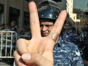 A Lebanese protester flashes the victory gesture while standing before a riot policeman at a security barrier across a road leading to the parliament headquarters during a demonstration in the capital Beirut's downtown district on November 19, 2019. An unprecedented protest movement against the ruling elite entered its second month with the country in the grip of political and economic turmoil. The leaderless pan-sectarian movement has swept the Mediterranean country since October 17, prompting the resignat