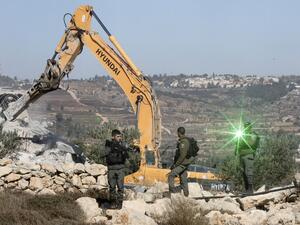 An Israeli border guard points a laser light at the camera as others keep watch while a bulldozer demolishes Palestinian houses near al-Arub camp, on the outskirts of the West Bank town of Hebron (AFP)