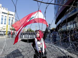 A Lebanese demonstrator waves the national flag while security forces stand by, during an anti-American protest near the US embassy in Awkar, northeast of the capital Beirut, on November 24, 2019. (ANWAR AMRO / AFP)