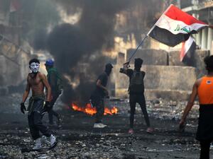 An Iraqi anti-government protester waves a national flag close to a concrete barricade amidst clashes with security forces along the capital Baghdad's Rasheed street near al-Ahrar bridge  (AFP)