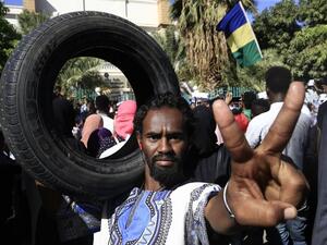Sudanese protester flashes the victory gesture while holding a car tire on his shoulder during a demonstration in the centre of Sudan's capital Khartoum outside the prime minister's offices (AFP)
