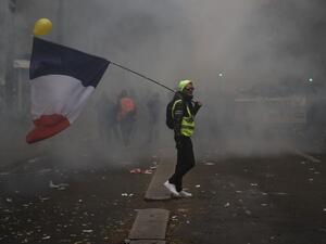 A man holding a French flag and a yellow vest walks in tear gas during a demonstration against the pension overhauls, in Paris, on December 5, 2019 as part of a nationwide strike. Trains cancelled, schools closed: France scrambled to make contingency plans on for a huge strike against pension overhauls that poses one of the biggest challenges yet to French President's sweeping reform drive. Zakaria ABDELKAFI / AFP