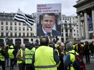 A protester holds a sign depicting French President and reading "Let them come and get me !" on the Place de la Bourse in Paris during a demonstration called by the "Gilets Jaunes" (Yellow Vests) movement on December 28, 2019, as part of a nationwide multi-sector strike against French government's pensions overhaul. STEPHANE DE SAKUTIN / AFP