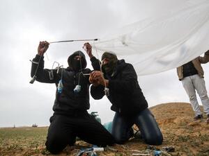 Young Palestinian men, masked in order to avoid being recognised, prepare a flammable object to be flown toward Israel, near the Israel-Gaza border east of Rafah in the southern Gaza Strip, on January 18, 2020. SAID KHATIB / AFP