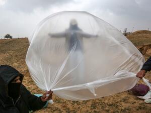 Young Palestinian men, masked in order to avoid being recognised, prepare a flammable object to be flown toward Israel, near the Israel-Gaza border east of Rafah in the southern Gaza Strip, on January 18, 2020. SAID KHATIB / AFP