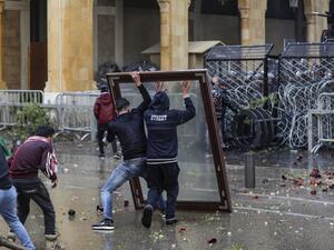 Anti-government protesters use a window as a makeshift shield as they confront security forces from behind a barbed-wire and metal fence barrier during clashes in the central downtown district of the Lebanese capital Beirut near the parliament headquarters on January 18, 2020. ANWAR AMRO / AFP