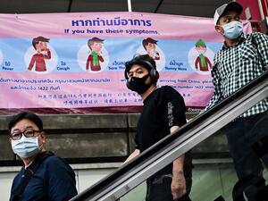 People wearing protective facemasks walk past a government health advisory campaign on the coronavirus infection prevention at a city commuter train station in Bangkok, on February 1, 2020. AFP