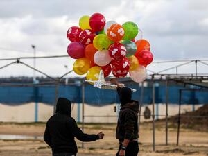 Masked Palestinians prepare to release an incendiary device near Gaza's Bureij refugee camp, along the Israel-Gaza border fence, on February 10, 2020. MAHMUD HAMS / AFP
