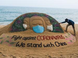 In this picture taken on February 10, 2020 Indian artist Sudarsan Pattnaik puts some final touches as he makes a sand sculpture depicting people wearing protective facemasks with a message reading 'Fight against coronavirus, We stand with China' at Puri beach in Puri. AFP