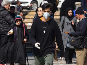 A young Iranian man wearing a protective mask and gloves, walks in a busy street in the capital Tehran on February 22, 2020. Iran today reported one more death among 10 new cases of coronavirus, bringing the total number of deaths in the Islamic republic to five and infections to 28. ATTA KENARE / AFP