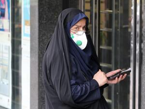 A woman wears a protective mask while using a smartphone as she stands along the side of a street in the Iranian capital Tehran on February 24, 2020. Iran's government vowed on February 24 to be transparent after being accused of covering up the deadliest coronavirus COVID-19 outbreak outside China as it dismissed claims the toll could be as high as 50. The authorities in the Islamic republic have come under mounting public pressure since it took days for them to admit to "accidentally" shooting down a Ukra