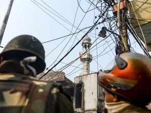 Security personnel stand guard on a road as a Hindu religious flag is seen on a minaret (C) of a burnt-out mosque following clashes between people supporting and opposing a contentious amendment to India's citizenship law in New Delhi on February 26, 2020. Four more people have died in some of the worst sectarian violence in decades in New Delhi, a hospital source told AFP, which takes the death toll from several days of rioting to 17. Sajjad HUSSAIN / AFP