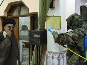 A civil defence worker motions to a Muslim cleric while disinfecting a mosque in the Ashar district of Iraq's southern city of Basra on March 7, 2020, as part of efforts against COVID-19 coronavirus disease. Hussein FALEH / AFP