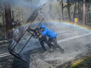 Migrants take cover behind a wooden board as Greek police uses water cannons to block them trying to break fences in the Turkey-Greece border province of Edirne on March 7, 2020. AFP/File