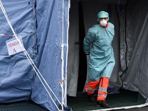 A hospital employees wearing a protection mask and gear exits a tent at a temporary emergency structure set up outside the accident and emergency department, where any new arrivals presenting suspect new coronavirus symptoms are being tested, at the Brescia hospital, Lombardy, on March 13, 2020. MIGUEL MEDINA / AFP