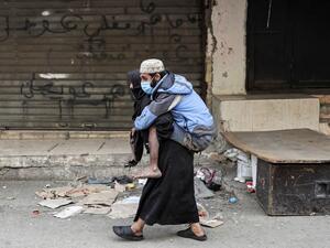 A woman carries a diabled man wearing a protective face mask in the market of the Palestinian refugee camp of Sabra, south of the capital Beirut, amid measures coordinated with Palestinian security forces to shut down all shops in a bid to limit the spread of the Covid-19 disease caused by the novel coronavirus, on march 22, 2020. ANWAR AMRO / AFP