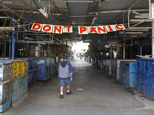 A man passes under a "Don't Panic" banner hanging at the entrance of Shuk HaCarmel (Caramel) market in the Israeli coastal city of Tel Aviv on March 24, 2020 after Israel barred residents from leaving home for non-essential reasons and stopped night-time public transport, tightening already strict measures to fight the spread of coronavirus. JACK GUEZ / AFP