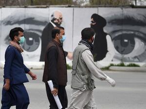 Men wearing facemasks as a precautionary measure against the COVID-19 novel coronavirus walk past a wall painted with images of US Special Representative for Afghanistan Reconciliation Zalmay Khalilzad (L) and Taliban co-founder Mullah Abdul Ghani Baradar (R), in Kabul April 5, 2020. WAKIL KOHSAR / AFP