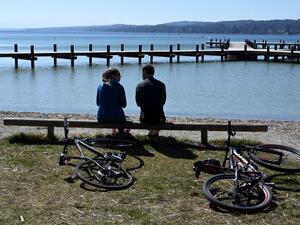 People sit in front of an empty swimming and sun pier near the shore of lake Starnberger See in Percha, southern Germany during warm weather with temperatures reaching 20 degrees celsius on April 5, 2020. AFP