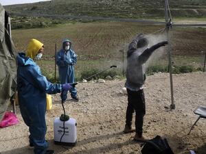 An employee at the Palestinian ministry of health sprays disinfectant on a worker returning from Israel through the Tarqumiah crossing, north-west of the West Bank city Hebron, on April 6, 2020, to stem the spread of the COVID-19 pandemic. HAZEM BADER / AFP