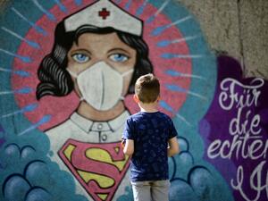 A boy stands in front of a graffiti painted by artist Kai 'Uzey' Wohlgemuth featuring a nurse as Superwoman on a wall in Hamm, western Germany, on April 8, 2020 refering to the spread of the novel coronavirus COVID-19. Ina FASSBENDER / AFP
