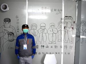 A security personnel stands in front of coronavirus themed drawings seen on a wall at the Leishenshan Hospital that had offered beds for coronavirus patients in Wuhan, in China’s central Hubei province on April 11, 2020. Noel Celis / AFP