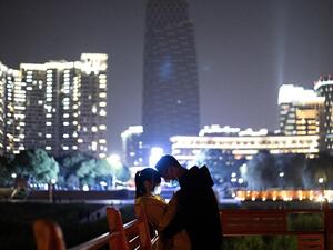 A couple wearing a facemask cuddles along a park at the Yangtze river in Wuhan, in China's central Hubei province early on April 12, 2020. NOEL CELIS / AFP