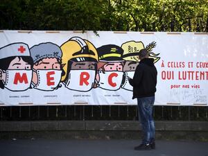 A man looks at a poster thanking the healthcare personnel, shopkeepers, the French national security, the post office staff members and farmers, in Paris, on April 14, 2020, on the twenty-nineth day of a lockdown in France to stop the spread of the COVID-19, (the novel coronavirus). FRANCK FIFE / AFP