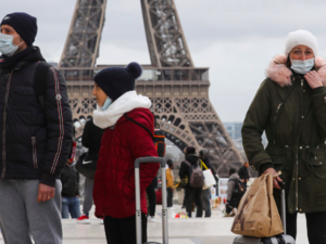People wear protective facemasks as they walk in front the Eiffel Tower, in Paris on March 12, 2020 | Ludovic Marin/AFP via Getty Images