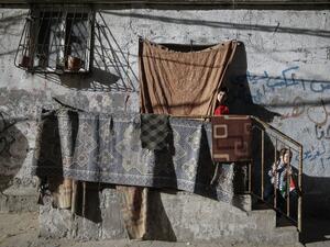 A Palestinian girl takes a peek from behind a curtain at her home's entrance as her sibling plays on the stairs, at al-Shati camp for Palestinians refugees, before sunset during the Muslim holy month of Ramadan, in Gaza City, on may 8, 2020, amid the COVID-19 pandemic. MOHAMMED ABED / AFP