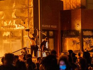 Flames from a nearby fire illuminate protesters standing on a barricade in front of the Third Police Precinct on May 28, 2020 in Minneapolis, Minnesota, during a protest over the death of George Floyd, an unarmed black man, who died after a police officer kneeled on his neck for several minutes. (AFP/File)