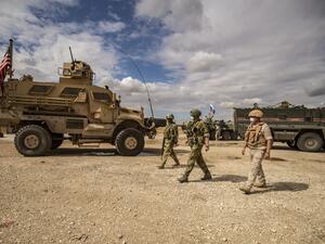 Russian soldiers walk past an US military vehicle along the M4 highway by the town of Tal Tamr on May 25, 2020, as they monitor the reopening of the road to civilian traffic between the border towns of Kobane and Tal Tamr for the first time since a Turkish-backed invasion last year saw the route closed. DELIL SOULEIMAN / AFP