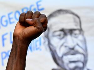 A man raises his fist in front of a portrait of George Floyd, an unarmed black man who died after a white policeman knelt on his neck during an arrest in the US, in Madrid, on June 7, 2020 during a demonstration against racism and in solidarity with the Black Lives Matter movement. Gabriel BOUYS / AFP