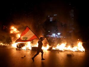 A protester holding the Lebanese flag runs as protesters block the Jounieh Tripoli highway with flaming tires set aflame during a demonstration against dire economic conditions in Jal el Dib North East of the Lebanese capital Beirut late on June 11, 2020. Patrick BAZ / AFP
