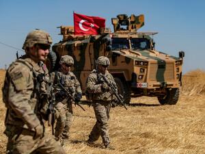 US troops walk past a Turkish military vehicle on the outskirts of Tal Abyad town along the Syrian-Turkish border on 8 September (AFP)