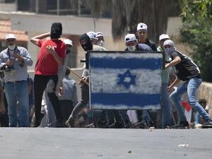 Palestinian protesters, standing behind a shield painted with the colours of the Israeli flag, hurl stones towards Israeli troops (unseen) during a demonstration in the village of Kfar Qaddum in the occupied West Bank against the Jewish state's plans to annex part of the Palestinian territory on July 3, 2020. JAAFAR ASHTIYEH / AFP