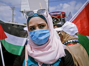 A Palestinian woman wearing a protective mask amid the COVID-19 pandemic lifts a national flag during a rally for supporters of the Fateh movement against Israel's West Bank annexation plans, in Beit Hanun in the north of the Gaza Strip, on July 6, 2020. MOHAMMED ABED / AFP