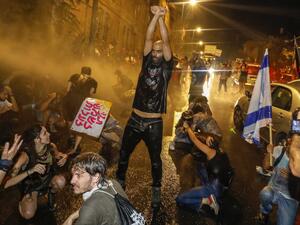 A protestor holds up his fists as Israeli police spray the crowd with water cannon during a rally against Prime Minister Benjamin Netanyahu in Jerusalem, on July 19, 2020 amid the coronavirus pandemic. Israeli police fired water cannons to disperse anti-government protests attended by thousands on Saturday, as public anger mounts over the handling of the coronavirus crisis. Demonstrators gathered outside Prime Minister Benjamin Netanyahu's residence in Jerusalem and at a park in Tel Aviv, voicing frustratio
