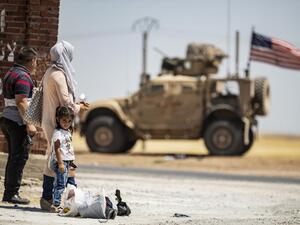 A family stands across a US military vehicle parked on the outskirts of Rumaylan (Rmeilan) in Syria's Kurdish-controlled northeastern Hasakeh province, on July 16, 2020. Delil SOULEIMAN / AFP