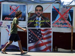 An Iraqi anti-government demonstrator walks past posters of Iraqi polititians and a US flag in Tahrir Square in the capital Baghdad, on August 1, 2020. AHMAD AL-RUBAYE / AFP