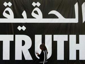 A file photo taken on April 5, 2005 shows a Lebanese woman using her mobile as she walks past a giant banner reading "truth" in Arabic and English in the Lebanese capital Beirut. A massive bomb tore through Hariri's armoured convoy as he drove home for lunch on Valentine's Day 2005, killing him and 21 other people including seven of his bodyguards, as well as wounding 226 others. A UN-backed court is to deliver its judgement on August 7, 2020, on four suspected Hezbollah members tried in absentia for former