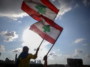 Lebanese women wave the national flag during a commemoration ceremony for the victims of the Beirut port explosion across from the capital's harbour, on August 11, 2020. PATRICK BAZ / AFP