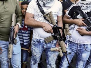 A youth peeks from behind between the shoulders of armed members of the Fatah movement, during a rally against the US-brokered UAE-Israel deal to normalise relations, at the Askar camp for Palestinian refugees east of Nablus in the occupied West Bank, on August 22, 2020. JAAFAR ASHTIYEH / AFP