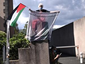 A woman holds a keffiyeh and a Palestinian flag as the pack rides during the 13th stage of the 107th edition of the Tour de France cycling race, 191 km between Chatel-Guyon and Puy Mary, on September 11, 2020. Marco BERTORELLO / AFP