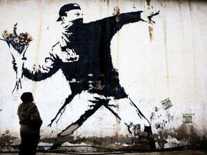 Two men sit in front of Banksy’s ‘Flower Thrower’ mural painted on a wall of a petrol station in the West Bank town of Bethlehem. (THOMAS COEX AFP/File)