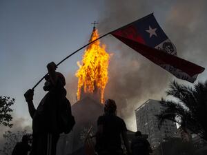 A demonstrator flutters a Chilean flag outside the burning church of Asuncion, set on fire by protesters, on the commemoration of the first anniversary of the social uprising in Chile, in Santiago, on October 18, 2020, as the country prepares for a landmark referendum. MARTIN BERNETTI / AFP A demonstrator flutters a Chilean flag outside the burning church of Asuncion, set on fire by protesters, on the commemoration of the first anniversary of the social uprising in Chile, in Santiago, on October 18, 2020, as the country prepares for a landmark referendum. MARTIN BERNETTI / AFP