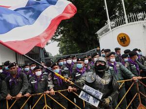 A royalist supporter waves a large Thai national flag in front of police standing guard during a rally outside the German embassy to show support for the Thai royal establishment in Bangkok on October 26, 2020. Jack TAYLOR / AFP