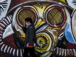 A man wearing a face mask as a preventive measure against the novel coronavirus COVID-19, walks by a graffiti in Bogota on August 25, 2020 Colombia will begin a new phase against the pandemic in September with "specific restrictions" and reactivation of economic sectors given the downward trend in infections,President Ivan Duque announced on August 24. Juan BARRETO / AFP